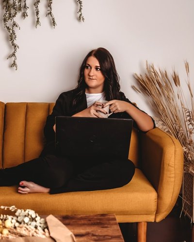 Katlin Pacheco sitting on a mustard-yellow sofa with a laptop and a mug